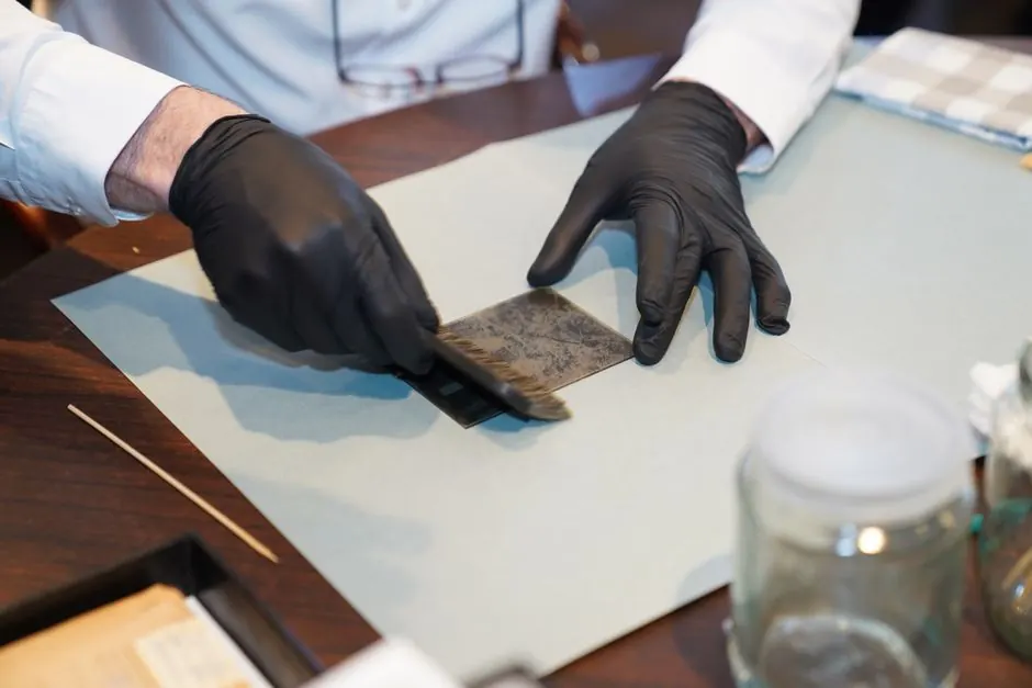 A restorer carefully working on a photograph with gloves and brush, focusing on details.